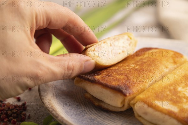Fried crispy pancakes with meat and cheese with hand on brown concrete background and linen textile. side view, close up, selective focus