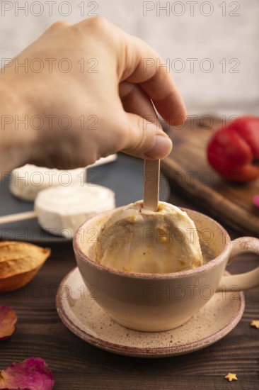?hocolate Ice cream in white glaze, cup of coffee, with hand on brown wooden background, side view, close up, selective focus