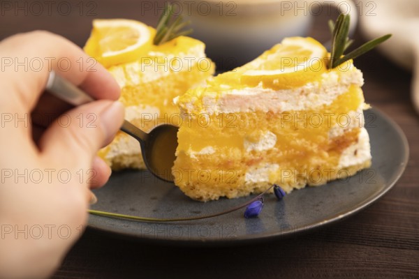 Lemon cake with hand on brown wooden background and linen textile, cup of coffee, side view, close up, selective focus