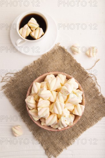 Orange and pink marshmallow in ceramic bowl on white wooden background and linen textile, top view, flat lay, copy space, minimalism