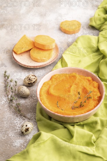 Sweet potato porridge in ceramic bowl on brown concrete background and green textile. Diet, healthy eating concept. side view, close up