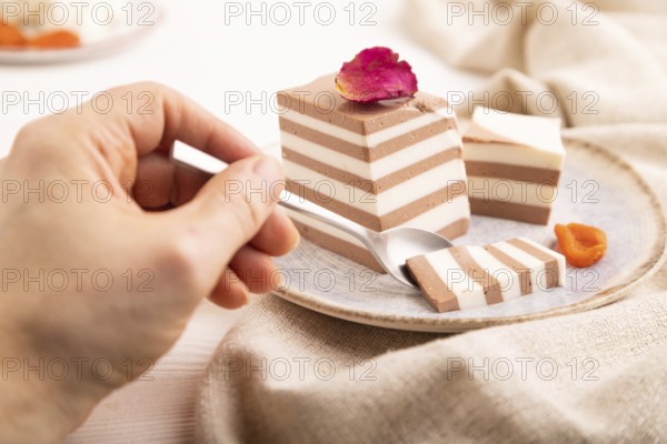 Cocoa and milk jelly with dried apricots with hand on white wooden background and linen textile, side view, close up, minimalism, selective focus