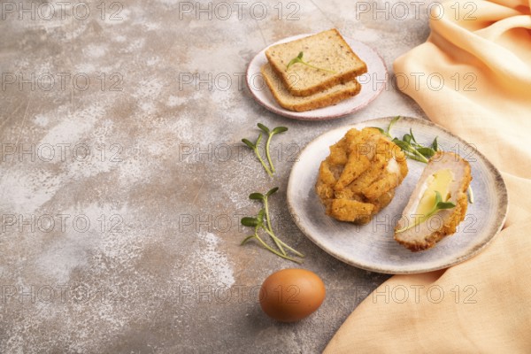 Chicken Schnitzel on blue plate with microgreen on brown concrete background and orange linen textile. side view, copy space