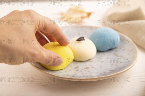 Japanese Mochi Cakes with hand on white wooden background and linen textile, side view, close up, selective focus