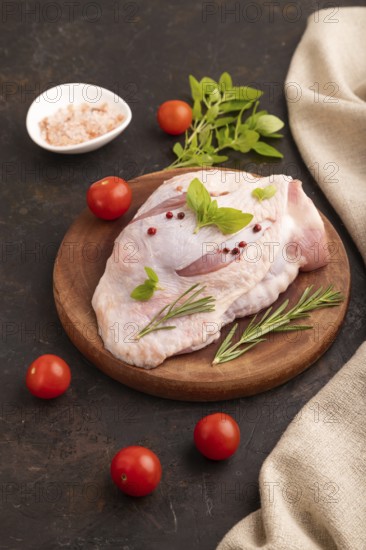 Raw Turkey Thigh with spices and rosemary on cutting board on black concrete background and linen textile. side view, close up