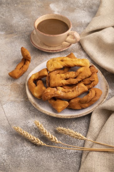 Crunchy biscuit Brushwood cookies sprinkled with powdered sugar on brown concrete background and linen textile, cup of coffee, side view, close up