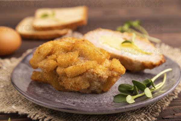 Chicken Schnitzel on gray plate with microgreen on brown wooden background and linen textile. side view, close up, selective focus