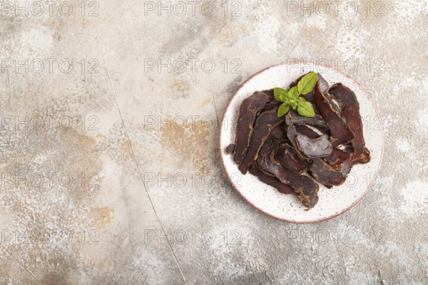 Armenian Basturma dried meat on plate with pepper and herbs on brown concrete background. Top view, flat lay, copy space