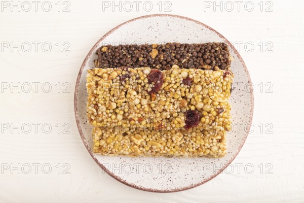 Granola bars with caramel, nuts, flakes in ceramic plate on white wooden background. Top view, flat lay, close up