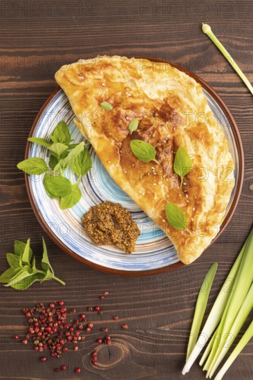 Fried homemade Khachapuri cake with cheese and meat, fried in pan. Traditional Georgian cuisine on brown wooden background. Side view, copy space