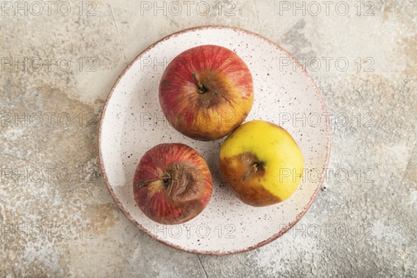 Decaying, Rotting apples on ceramic plate on brown concrete background. Top view, copy space, flat lay, minimalism
