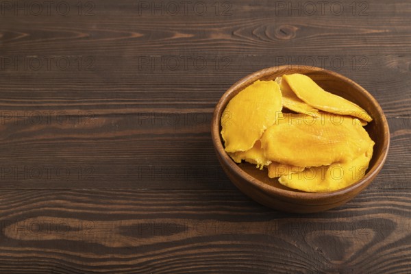 Dried Mango in wooden bowl on brown wooden background. Side view, copy space. healthy food, minimalism