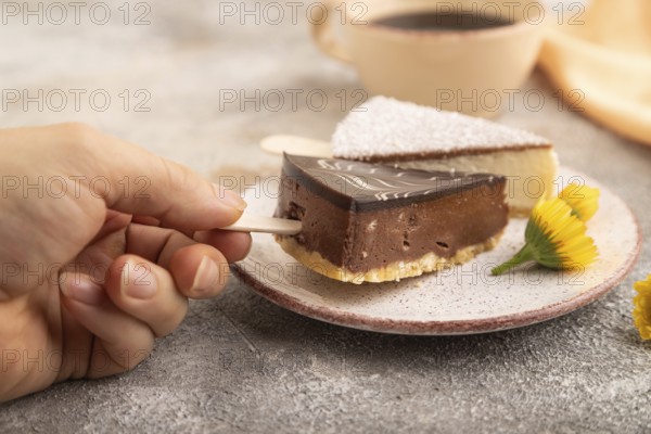 Chocolate and Vanilla Cake pops Marshmallow with hand with cup of coffee on brown concrete background and orange linen textile. side view, close up, selective focus hold