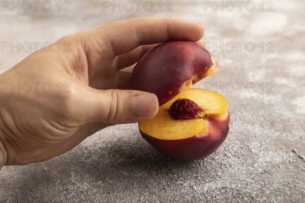 Peach Cut in half with hand on brown concrete background. Side view, copy space. healthy food, vegetable, minimalism