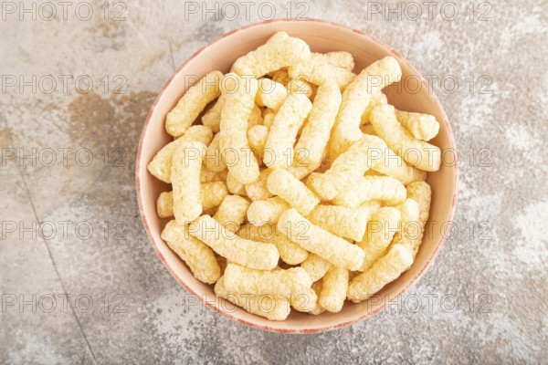 Corn flakes sticks with caramel in ceramic bowl on gray concrete background. Top view, flat lay, copy space