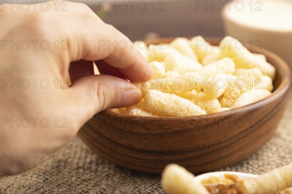 Corn flakes sticks with caramel in wooden bowl with hand on brown wooden background and linen textile. Side view, close up, selective focus