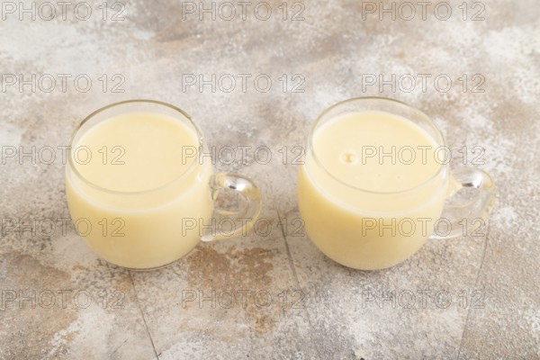 Organic non dairy banana and soy milk in glass on brown concrete background. Vegan healthy food concept, side view, close up