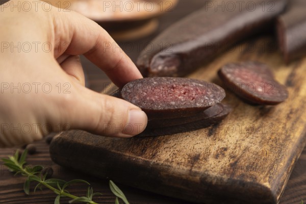 Sujuk sausage with hand on wooden cutting board with pepper and herbs on brown wooden background. Side view, close up, selective focus