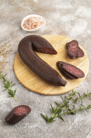 Sujuk sausage on wooden cutting board with pepper and herbs on brown concrete background. Side view, close up
