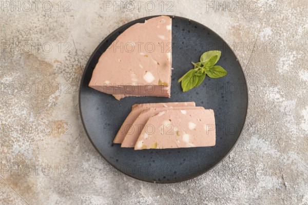 Mortadella sausage on plate with pepper and herbs on brown concrete background. Top view, flat lay, copy space