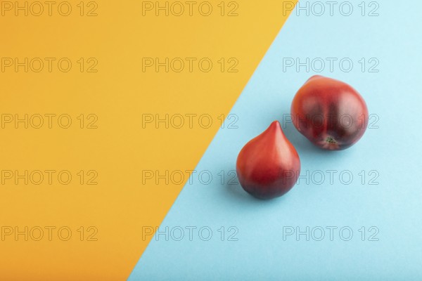 Red Heart shape tomatoes on blue and orange pastel paper background. Side view, copy space. healthy food, vegetable, minimalism