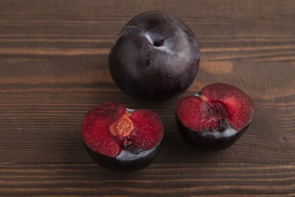 Purple Plum Cut in half on brown wooden background. Side view, close up. healthy food, vegetable, minimalism
