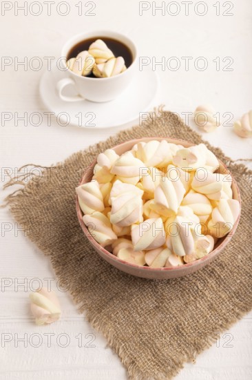 Orange and pink marshmallow in ceramic bowl on white wooden background and linen textile, side view, close up, minimalism