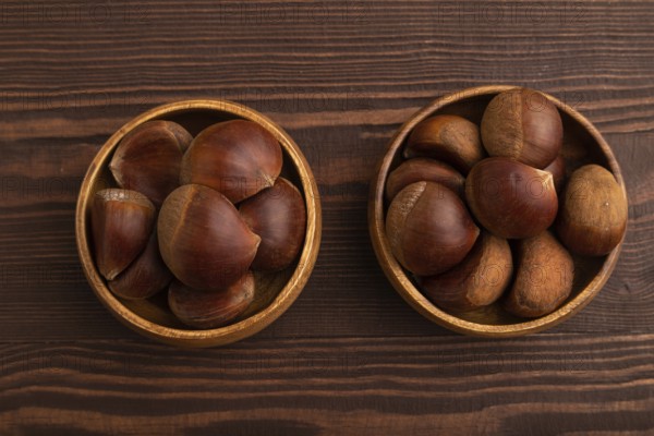Wooden bowl with raw edible ?hestnuts on brown wooden background, top view, flat lay, close up, minimalism
