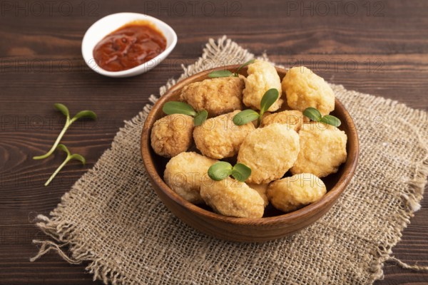 Fried crispy Chicken Nuggets with ketchup, microgreen on brown wooden background and linen textile. side view, close up