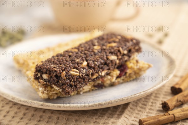 Granola bars with caramel, nuts, flakes in ceramic plate on brown concrete background, beige linen napkin, cup of green tea. Side view, close up, selective focus