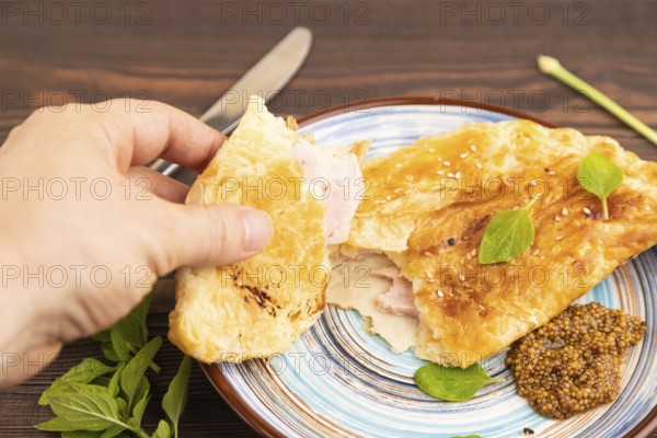 Fried homemade Khachapuri cake with cheese and meat, fried in pan with hand. Traditional Georgian cuisine on brown wooden background. Side view, close up, selective focus