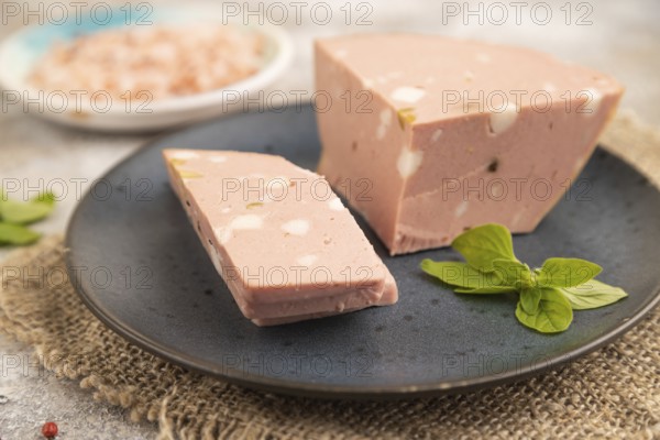 Mortadella sausage on plate with pepper and herbs on brown concrete background and linen textile. Side view, close up, selective focus