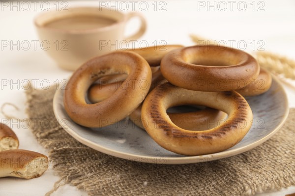 Homemade Ring Bagel with cup of coffee on white wooden background and linen textile. side view, close up, selective focus