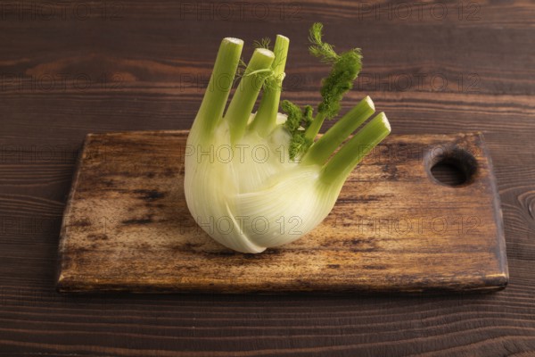 Fresh Fennel bulb on wooden cutting board on brown wooden background, side view, close up, minimalism