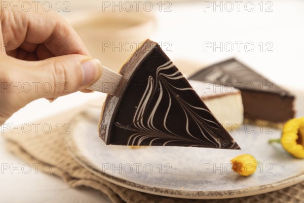 Chocolate and Vanilla Cake pops Marshmallow with hand with cup of coffee on white wooden background and beige linen textile. side view, close up, selective focus hold