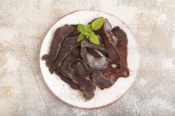 Armenian Basturma dried meat on plate with pepper and herbs on brown concrete background. Top view, flat lay, copy space