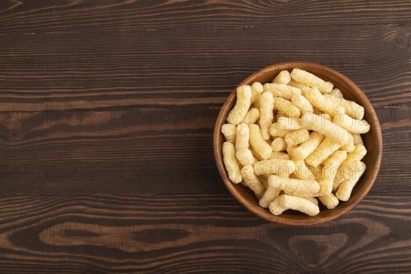 Corn flakes sticks with caramel in wooden bowl on brown wooden background. Top view, flat lay, copy space