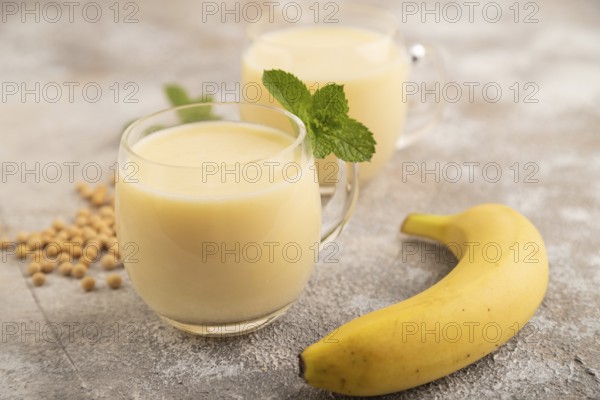 Organic non dairy banana and soy milk in glass on brown concrete background. Vegan healthy food concept, side view, close up, selective focus