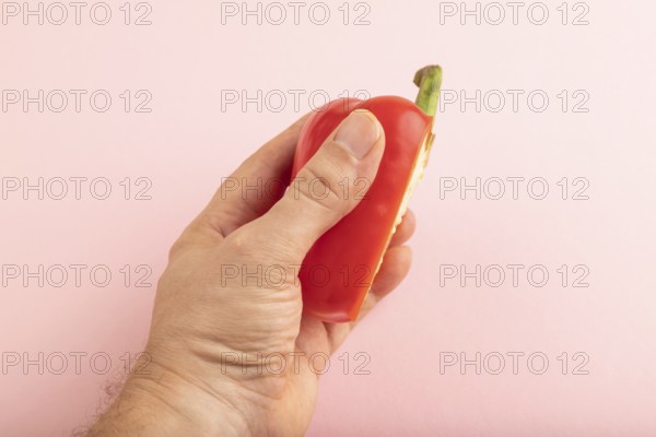 Hand holding sliced Red Cutted pepper on pink pastel background. Side view, copy space. Tropical, healthy food, vegetable, minimalism