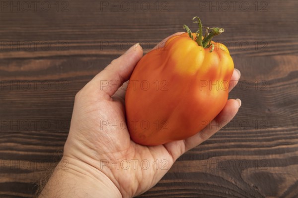 Red Heart Shape tomato with hand on brown wooden background. Top view, flat lay, close up. healthy food, vegetable, minimalism