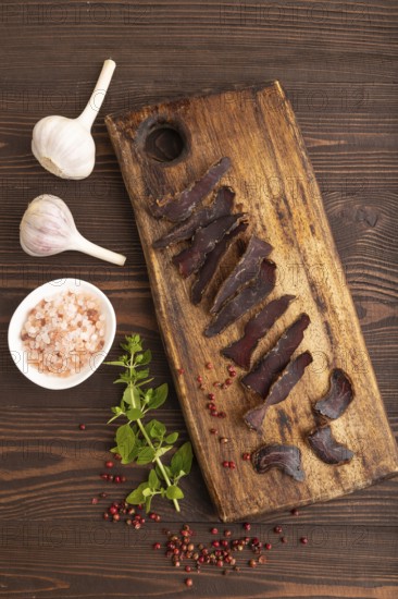 Armenian Basturma dried meat on wooden cutting board with pepper and herbs on brown wooden background. Top view, flat lay, copy space