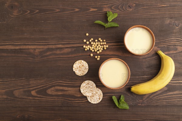 Organic non dairy banana and soy milk in clay cup on brown wooden background. Vegan healthy food concept, flat lay, top view, copy space