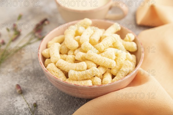 Corn flakes sticks with caramel in ceramic bowl on gray concrete background and orange linen textile. Side view, close up