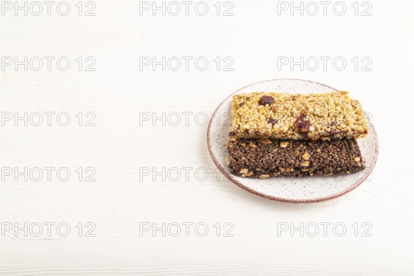 Granola bars with caramel, nuts, flakes in ceramic plate on white wooden background. Side view, copy space