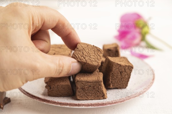 Chocolate marshmallow with cup of coffee with hand on white wooden background. side view, close up, selective focus