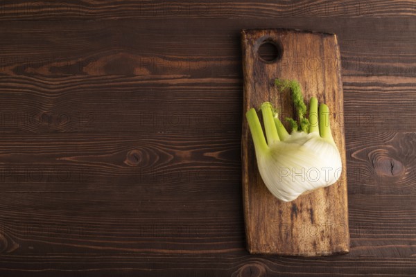 Fresh Fennel bulb on wooden cutting board on brown wooden background, top view, flat lay, copy space, minimalism