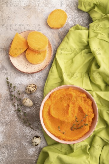 Sweet potato porridge in ceramic bowl on brown concrete background and green textile. Diet, healthy eating concept. top view, flat lay, close up