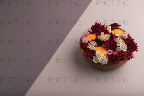 Wooden bowl with carrot slices and red Chrysanthemum flowers, Astrantia flowers, flower salad on beige and gray pastel paper background, side view, copy space, minimalism