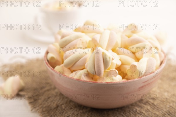 Orange and pink marshmallow in ceramic bowl on white wooden background, side view, close up, minimalism, selective focus