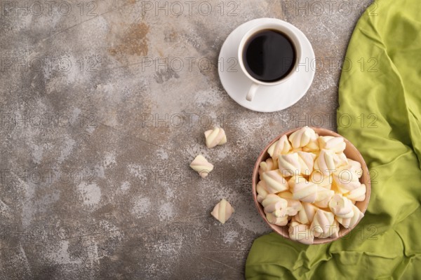 Orange and pink marshmallow in ceramic bowl on brown concrete background and green textile, top view, flat lay, copy space, minimalism